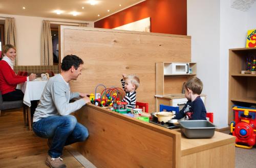 a man sitting at a counter with two children playing with toys at Naturhotel Bauernhofer in Heilbrunn