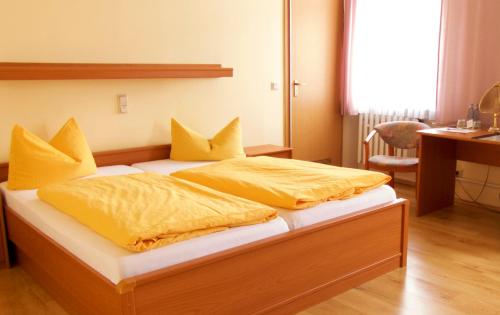Schlafzimmer mit einem Bett mit gelber Bettwäsche und einem Schreibtisch in der Unterkunft Hotel zum Schwan in Nachterstedt