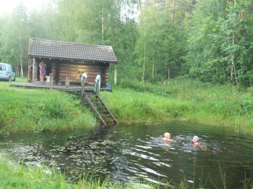 two people swimming in a pond in front of a cabin at Kauksi Puhkemaja in Kauksi