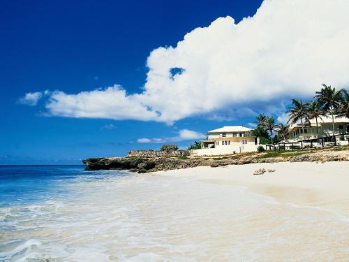 a beach with a house and palm trees and the ocean at Inchcape Seaside Villas in Christ Church
