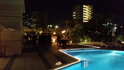 a group of people standing around a pool at night at Moon Ocean Ginowan Hotel & Residence in Ginowan