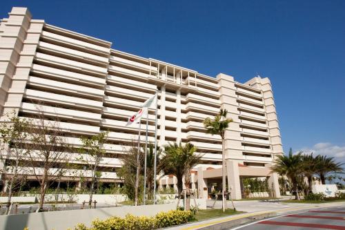 a large white building with palm trees in front of it at Moon Ocean Ginowan Hotel & Residence in Ginowan