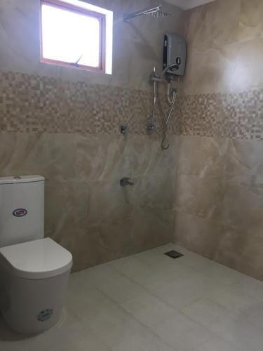 ein Bad mit einem WC, einem Fenster und einer Dusche in der Unterkunft Blue Wings Beach Hotel in Trincomalee