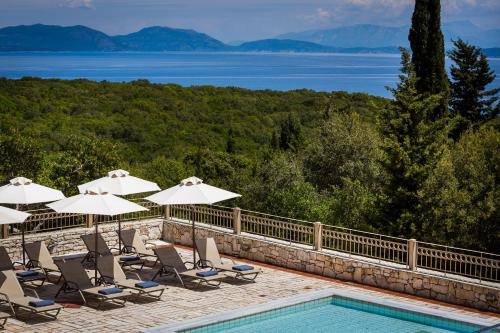 a pool with chairs and umbrellas next to the water at Almyra Hotel in Fiskardho