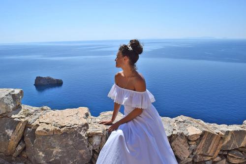 a woman in a white dress standing on a cliff at Aegialis Hotel & Spa in Aegiali