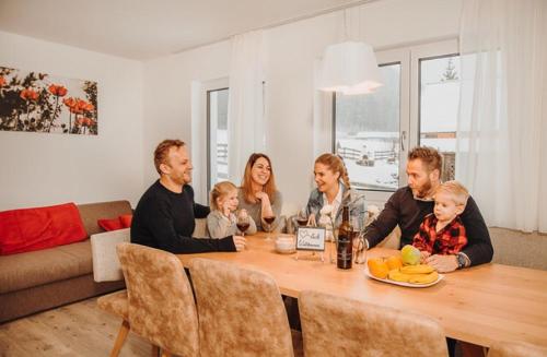 a family sitting around a wooden table in a living room at Appartements Almnest in Schladming