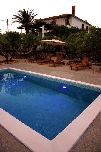 a blue swimming pool with chairs and an umbrella at Tvrdic Honey in Grohote