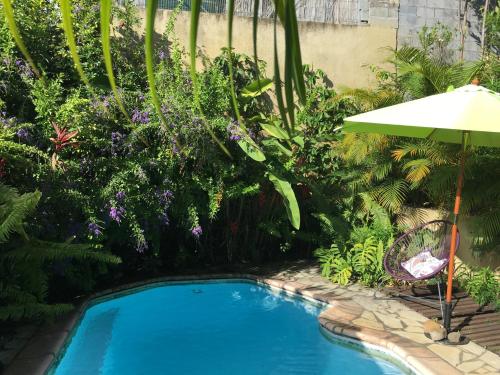 a swimming pool with an umbrella and some plants at Le Chalet dAZAE in La Rivière