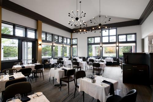 a restaurant with white tables and chairs and windows at Manoir des Sables Hôtel & Golf in Magog-Orford