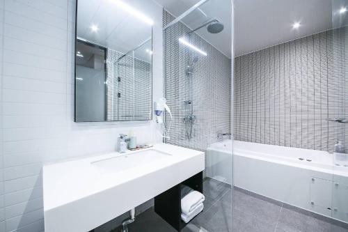 a white bathroom with a sink and a tub and a mirror at Golden River Hotel in Gwangmyeong