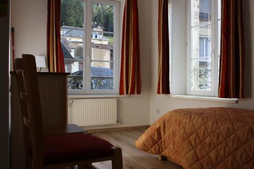 - une chambre avec deux fenêtres, un lit et une chaise dans l'établissement Résidence Maison Blanche, à Plombières-les-Bains