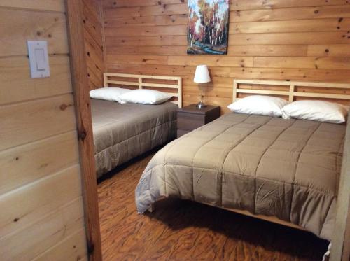 two beds in a room with wooden walls at Madawaska Lodge in Madawaska