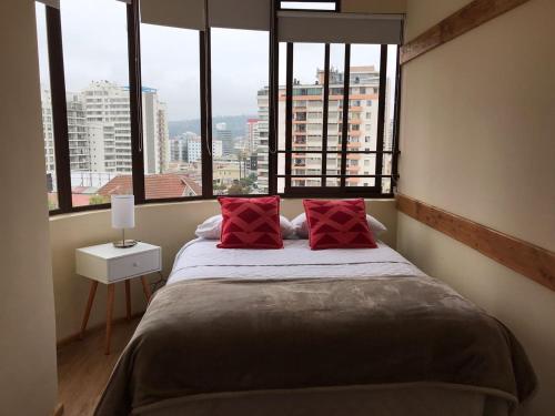 1 cama con almohadas rojas en una habitación con ventanas en Hostal My House, en Viña del Mar