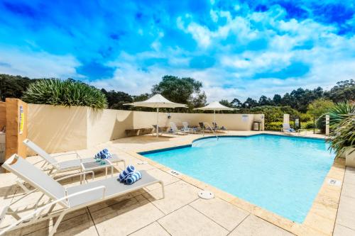 a swimming pool with white lounge chairs and a swimming poolvisorvisor at Grand Mercure Basildene Manor in Margaret River Town