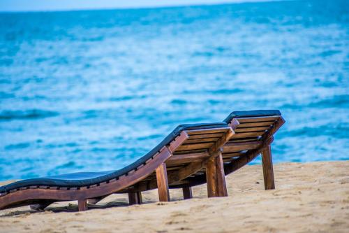 a wooden bench sitting on the beach near the water at Omeesha Beach Hotel in Kalpitiya