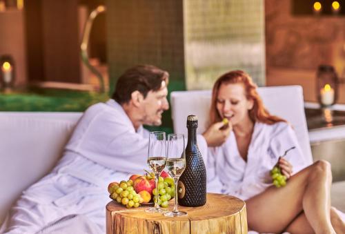 a man and woman sitting in a bed with a table with wine glasses at Hotel Pošta in Demanovska Dolina