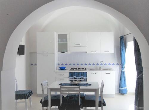 オストゥーニにあるMasseria Di Benedettoの白いキャビネット、テーブルと椅子付きのキッチンが備わります。