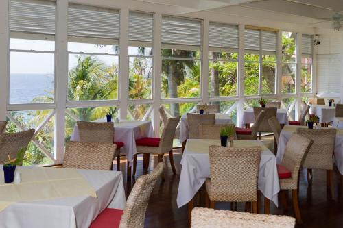 a restaurant with white tables and chairs and windows at Blue Haven Hotel - Bacolet Bay - Tobago in Scarborough