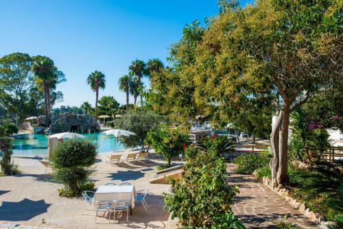 un resort con piscina con tavoli, sedie e alberi di Eden Resort Country a Torre San Giovanni Ugento