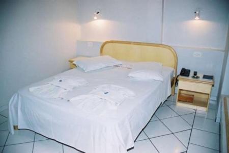 1 dormitorio con cama blanca y mesita de noche en Hotel Topazio Ltda, en Umuarama