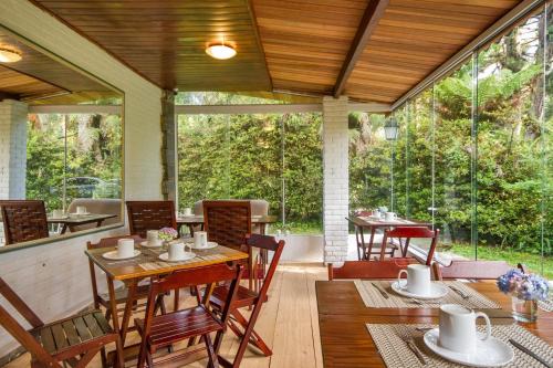 a screened porch with tables and chairs and windows at Villa Vintage Campos - Piscina e opções de suites com hidromassagem in Campos do Jordão