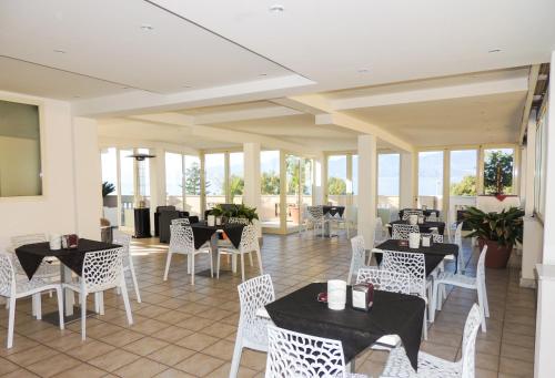 a restaurant with tables and white chairs and windows at Hotel Lungomare in Reggio Calabria