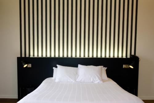 Hôtel & Spa Le Moulin de Moissac في مواساك: سرير مع اللوح الأمامي الأسود ووسائد بيضاء