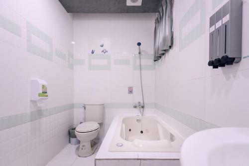 a white bathroom with a toilet and a bath tub at Guest Motel- Zhongli Branch in Pingzhen