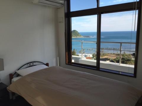 a bedroom with a large window with a view of the ocean at The Little Garden in Miyazaki