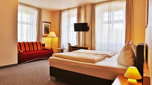 アルツァイにあるHotel Am Schlossのベッドと赤いソファが備わるホテルルームです。