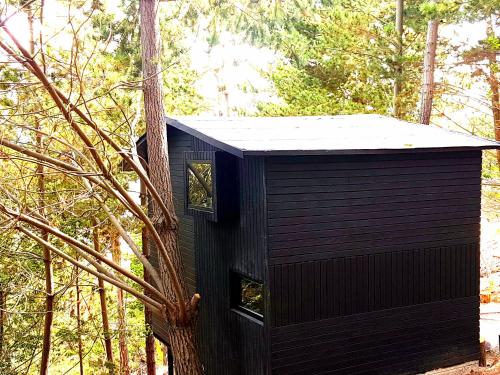 a black tree house in the middle of a forest at La Quinta Glamping - Lago de Tota in Cuítiva
