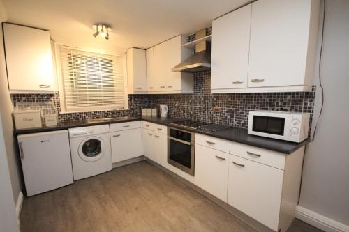cocina con armarios blancos, lavadora y secadora en The Garden Apartment en Leamington Spa