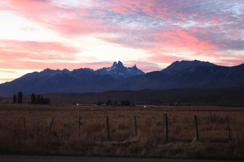una puesta de sol sobre un campo con montañas en el fondo en Los Tres Picos en Cholila
