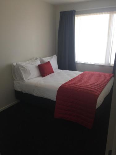 a bedroom with a bed with a red blanket and a window at Rolleston Highway Motel in Rolleston