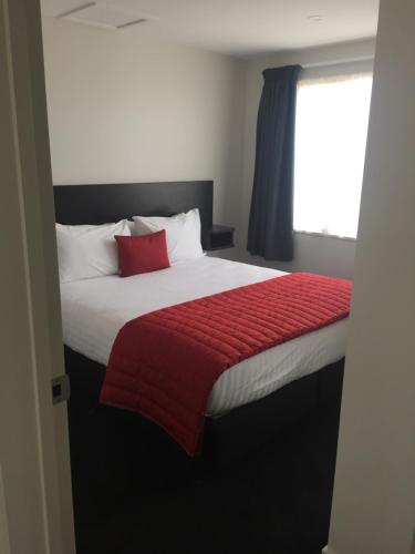 a bedroom with a bed with a red blanket and a window at Rolleston Highway Motel in Rolleston