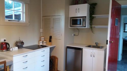 eine Küche mit weißen Schränken, einer Spüle und einer Mikrowelle in der Unterkunft Little Red School House in Oamaru