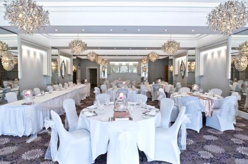 a banquet hall with white tables and chairs and chandeliers at Thornton Hall Hotel & Spa in Heswall