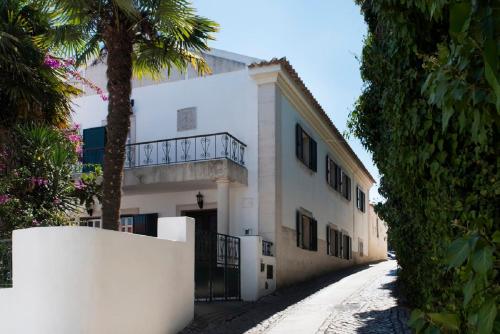 a white building with a balcony and a palm tree at Casa do Castelo in Santiago do Cacém