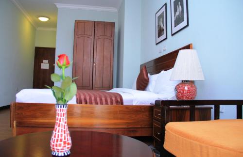 a bedroom with a bed and a vase with a flower on a table at Hotel Lobelia in Addis Ababa