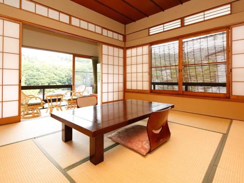 a room with a wooden table in a room with windows at 源泉掛け流しの宿Albergo湯楽 in Yugawara