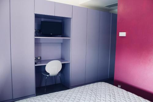 サンタルカンジェロ・ディ・ロマーニャにあるVilla Gretaの紫の壁の客室で、白い椅子とテレビが備わります。