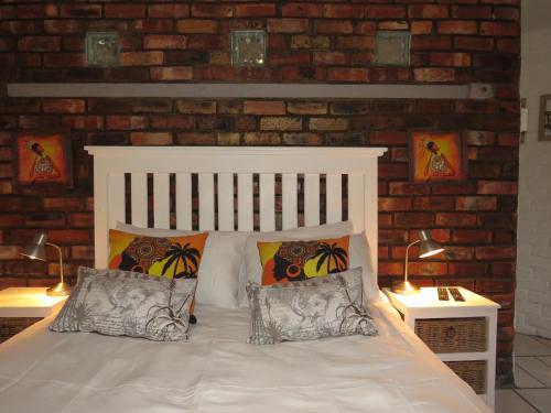 a bedroom with a white bed with a brick wall at Wiltshire Rondavel in Port Alfred