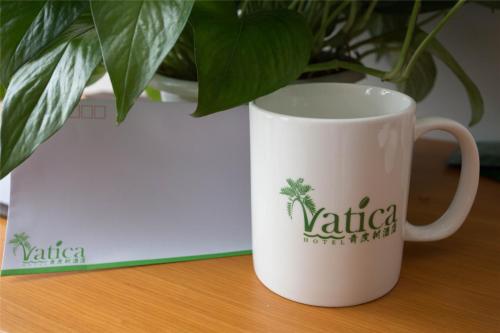 a white coffee mug sitting on a table next to a plant at Vatica Hefei Yaohai District Linquan Road Anhui Big Market Hotel in Hefei