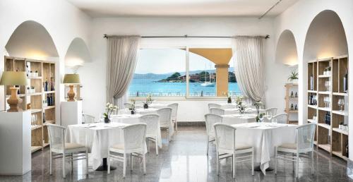 a restaurant with white tables and chairs and a large window at Gabbiano Azzurro Hotel & Suites in Golfo Aranci
