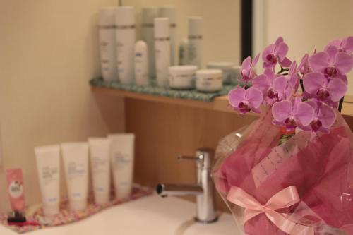 a vase of purple flowers sitting on a bathroom sink at Guesthouse COCO Hiroshima (Female Only) in Hiroshima