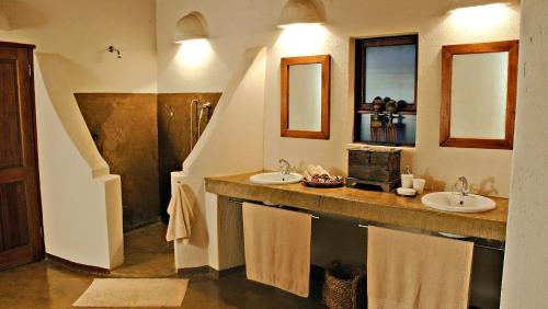 a bathroom with two sinks and two mirrors at Nyati Safari Lodge in Hoedspruit