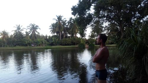 a man standing in front of a body of water at Priyanna Guest, Forest view in Polonnaruwa