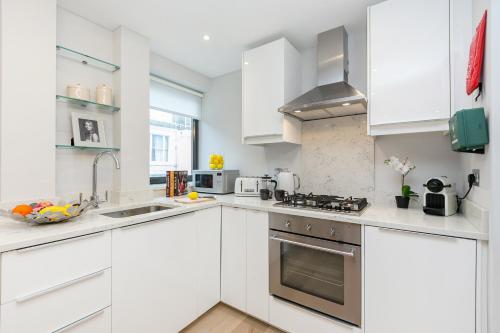 una cocina blanca con armarios blancos y fregadero en Three-Bedroom Bohemian Haven, en Londres
