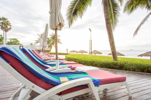 a row of lounge chairs and umbrellas on a beach at Novotel Rayong Rim Pae Resort in Klaeng