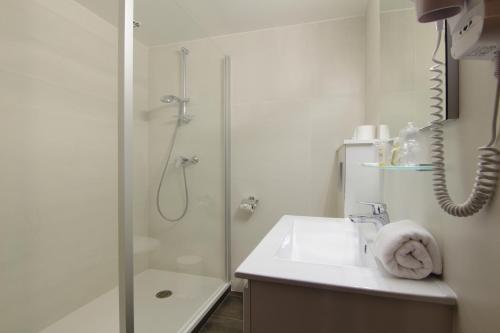 a white bathroom with a shower and a sink at Hôtel La Couleuvrine Sarlat Centre Ville in Sarlat-la-Canéda